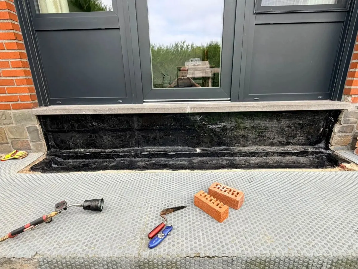 Membrane d'étanchéité bitumineuse soudée sous le seuil d'une porte-fenêtre, pendant les travaux de Plomberie-Toiture MERTENS B.
