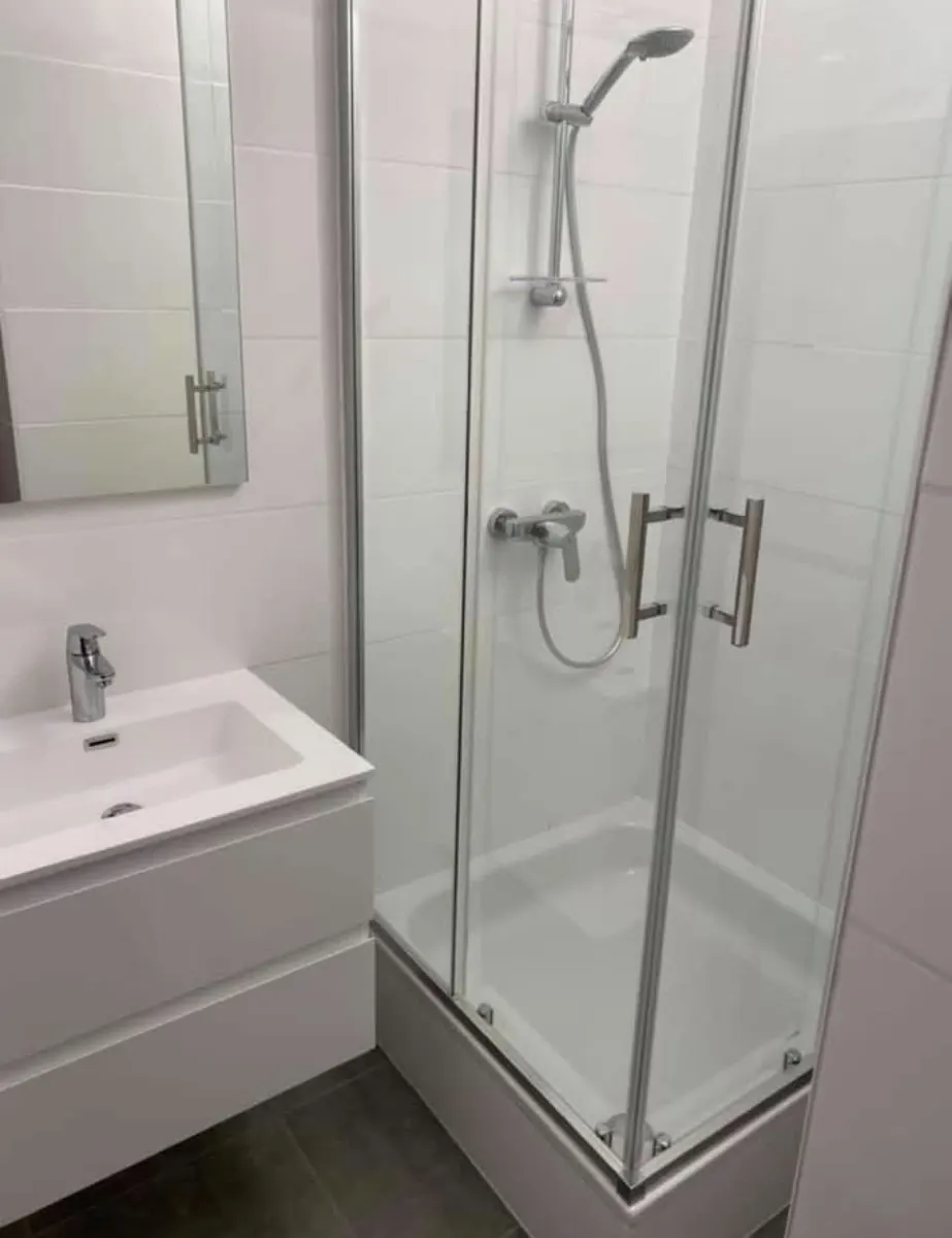 Salle de douche terminée avec cabine vitrée, colonne de douche et meuble-lavabo installés par Plomberie-Toiture MERTENS B.