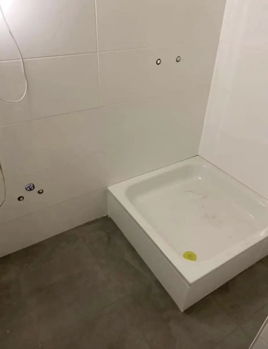 Receveur de douche posé et raccordements en attente dans une salle de bain carrelée, avant finition par Plomberie-Toiture MERTENS B.
