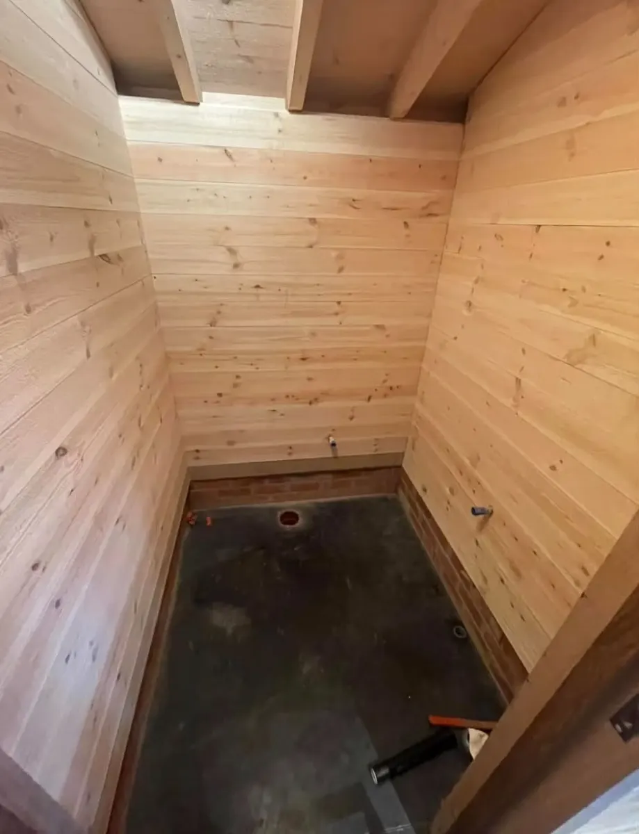 Petite pièce habillée de bois avec arrivées d'eau et évacuation prêtes, avant l'installation des sanitaires par Plomberie-Toiture MERTENS B.